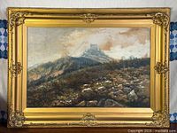 Framed mountain landscape watercolour in gilt frame on wall
