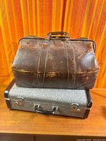 Both suitcases stacked; brown leather bag resting on blue fabric suitcase