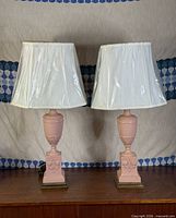 Full view of both pink neoclassical lamps with shades on wood surface
