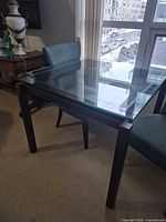 Full view of square glass table with glass top and dark brown metal legs