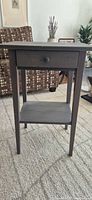 Front view of gray IKEA end table showing drawer, shelf, legs