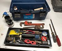 Toolbox open showing contents: pipe wrenches, file, screwdriver, tray with small tools and hardware