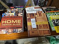 Group of books on table showing Home Repair Guide, Fine Woodworking cover, Maker’s Hand and garden title