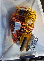 bin containing yellow halogen work light, handheld cage light, clamp light and multiple coiled orange extension cords