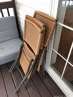 Four folded wicker patio chairs leaning against wall