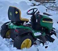 Left rear and side view of tractor in snow showing overall condition, torn seat, rear tires, mower deck