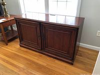 Front view of dark cherry veneer TV stand with two paneled doors closed.