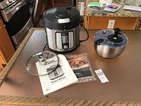 Full lot overview showing multi-cooker, salad spinner bowl, glass lid, manuals