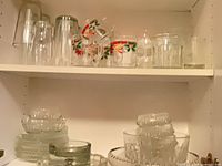 Cabinet shelf with mixed glassware: bowls, mugs with floral print, tumblers, pitcher