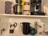 Cabinet shelf showing Braun coffee maker, French press, grinder, filters, mugs, creamer, sugar bowl