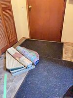 Stacked boot trays, rolled rag rugs on top, black entry mat underneath