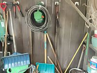 Overall view of hanging long-handled tools, hose on hanger and some hand tools
