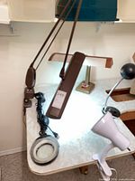 Multiple adjustable lamps on work surface including brown swing-arm lamp, magnifying lamp, white lamp