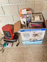 Group shot showing red clock radio on black radio beside box of cassettes and CDs with camera on floor