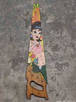 Painted side of hand saw showing artwork and handle