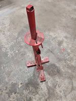 Full view of red manual tire changer stand on concrete floor