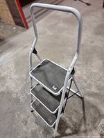 Front view of white 3-step folding ladder showing all steps and hand rail