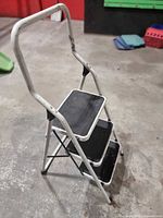 Full view of folded three-step ladder showing frame and handrail