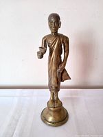 Front view of bronze standing monk statue with alms bowl on pedestal base