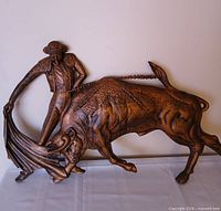 Front view of copper-tone matador and bull plaque