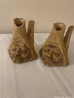 Front view of both carved wooden candle holders with faces visible