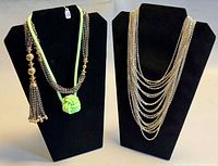 Two necklaces displayed: green knot pendant with accompanying beaded tassel chain, and stacked silver chain necklace on adjacent bust