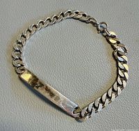 Full view of bracelet laid flat showing curb links, plate and clasp