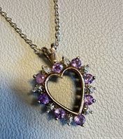 Front view close-up showing heart shape, amethyst stones, clear accents, and silver setting