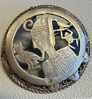 Front view of round silver brooch showing Nefertiti profile and motifs