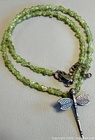 Full view of peridot chip necklace coiled showing dragonfly pendant and clasp