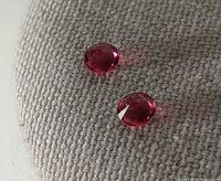 Two round reddish-pink faceted gemstones on fabric background