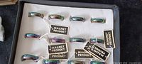 Box containing 21 iridescent magnetic hematite rings with tags