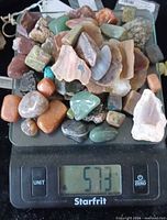Digital scale displaying 573 g with assorted polished and raw gemstones piled on platform
