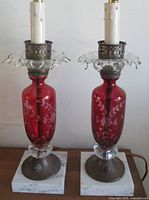 Front view of both cranberry cut-to-clear lamps on marble bases