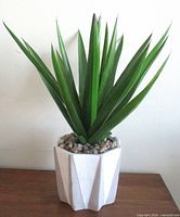 Full view of faux dracaena plant in white faceted planter