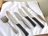 Six utensils on white cloth: four Ikea knives, wide silver fork, carving fork