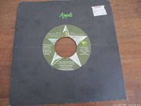 Front of 7" single in black Apple sleeve showing label through center hole
