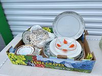 Overview of box showing assorted plates, glass plate, metal trivets