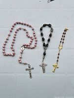 Three rosaries laid out: pink full rosary, black chaplet, burgundy chaplet