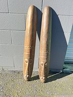 Pair of elongated carved wooden masks leaning against wall