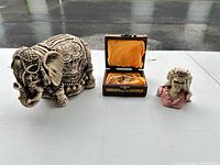 Overall view of elephant figurine, trinket box open with contents, skull bust