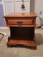Front view of wooden nightstand showing drawer, open shelf, bracket feet