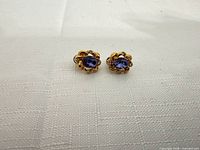 Front view of the pair of earrings showing purple stones and yellow gold floral settings