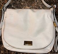 Front view of white leather bag with flap, zipper trim, logo plate, strap