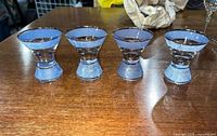 Four blue-purple shimmery shot glasses on a wooden surface, showing shape and color.
