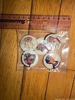 Bag containing five round American Girl Grin Pins beside ruler for scale