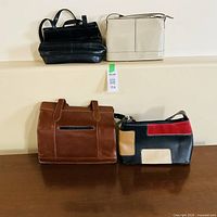 Four leather handbags in black, cream, brown, and black with red/beige panels displayed on table