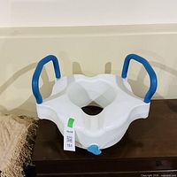 Front view of raised toilet seat showing blue grip handles and seat opening