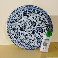 Front view of blue and white decorative plate with attached wall hanger and lot tag