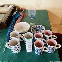 Group shot: seven mugs, shallow dish, white bowl, blue goblet on table